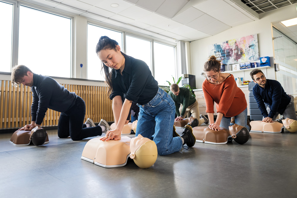 Kollegor som tillsammans övar bröstkompressioner på varsin Little Anne Gen2 HLR-docka under en gemensam HLR-kurs.
